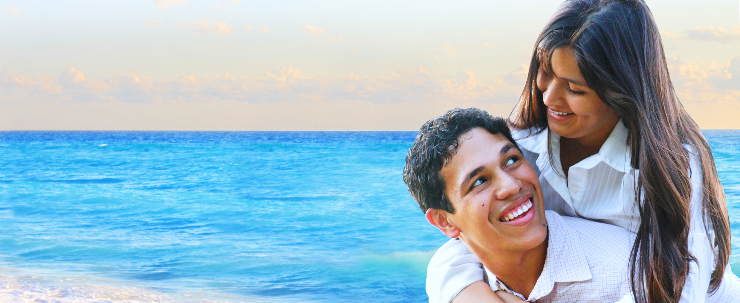 smiling couple with their arms around each other standing on a beach by the ocean